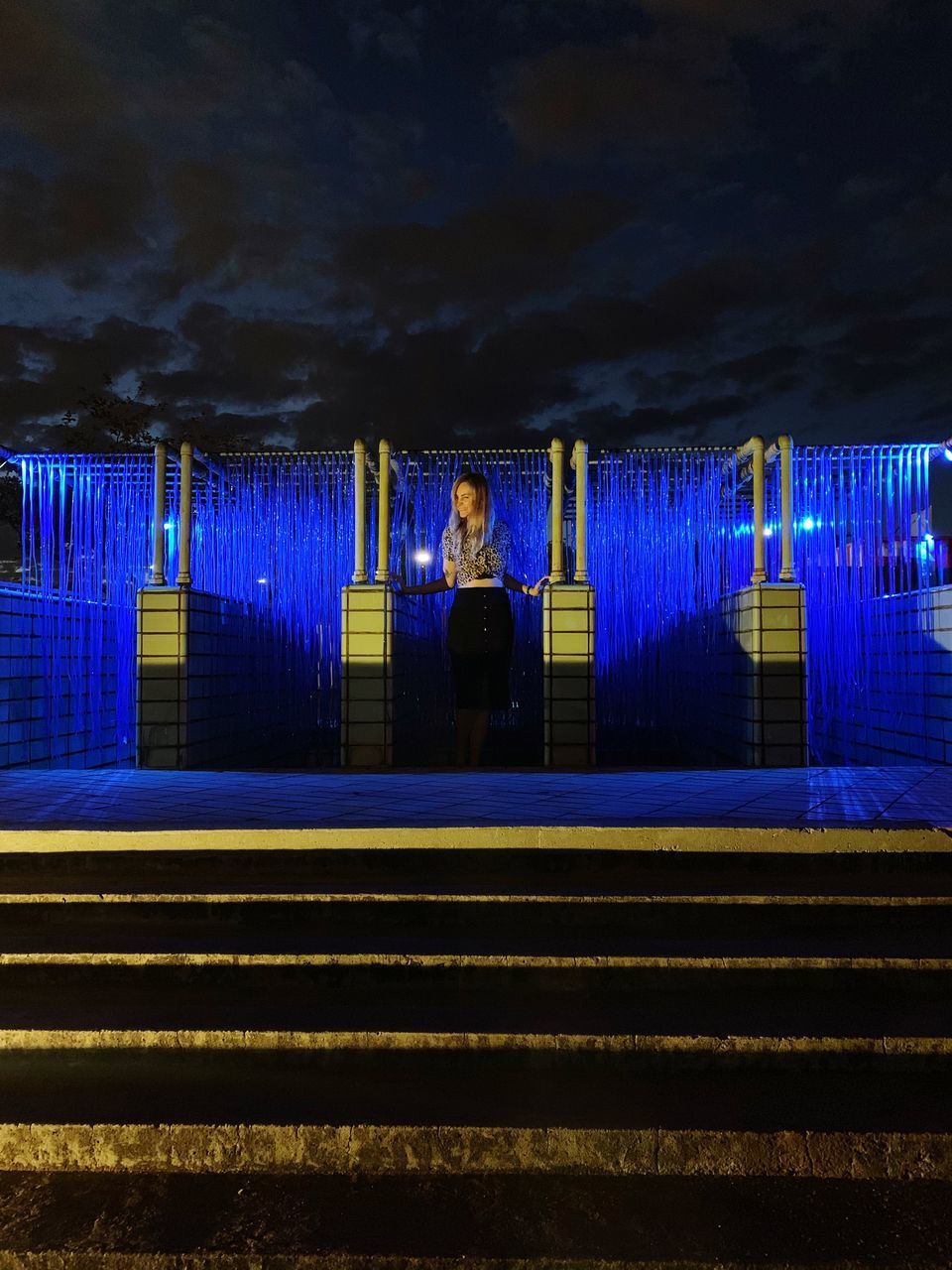 MAN STANDING BY ILLUMINATED LIGHTS AT NIGHT