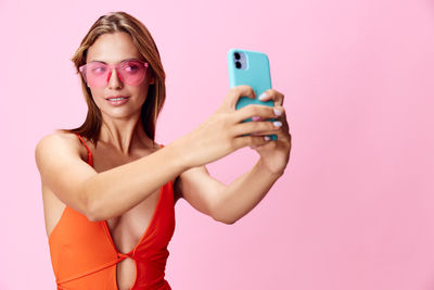 Young woman using mobile phone against pink background