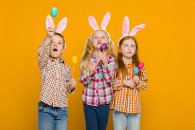 Portrait of siblings playing with toys against yellow background