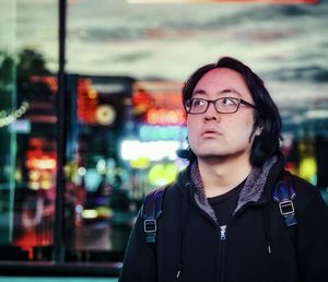 Portrait of young asian man in eyeglasses standing outside in city at night