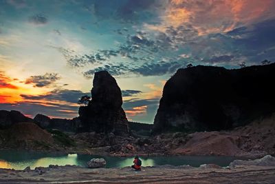 Woman standing on cliff by sea against sky during sunset