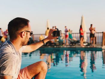 Man photographing by swimming pool against sky