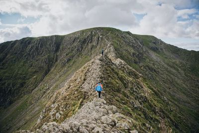 Men hiking on mountain against cloudy sky