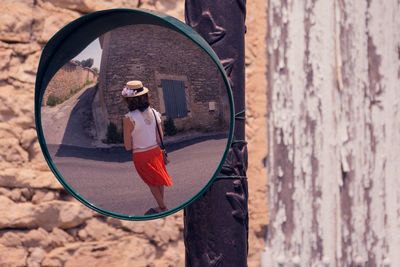 Woman reflecting on circular road mirror on pole