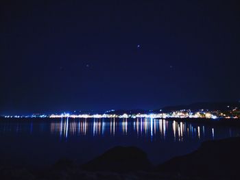 Illuminated city by lake against sky at night