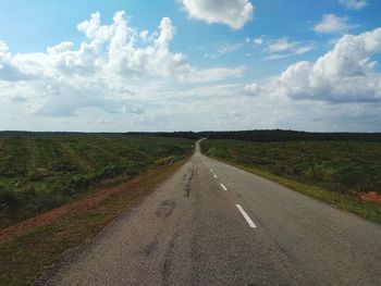Empty road amidst field against sky