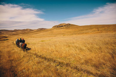 Men riding horse on field against sky