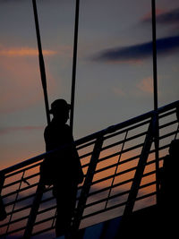 Low angle view of silhouette man standing on railing against sky