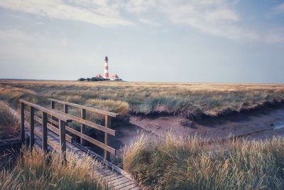 Lighthouse on field by building against sky