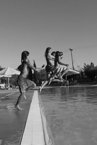 Young woman jumping in swimming pool against clear sky
