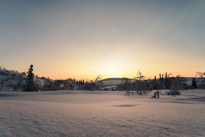 Snow covered field against sky during sunset