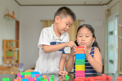 Brother and sister stacking toy blocks on table at home 