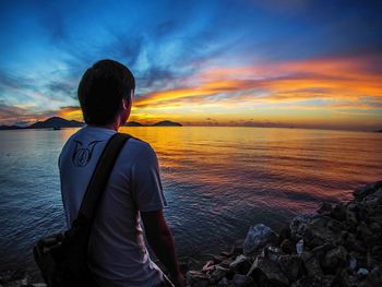 Rear view of man standing at beach during sunset