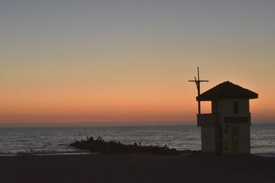 Lighthouse by sea against sky during sunset