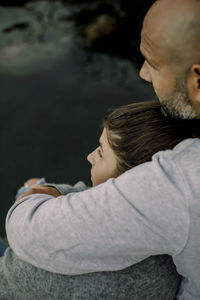 Father and daughter looking away while sitting by lake