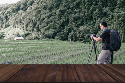 Side view of man holding camera on tripod on rice paddy