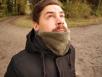 Close-up of mid adult man looking up while standing on dirt road in forest