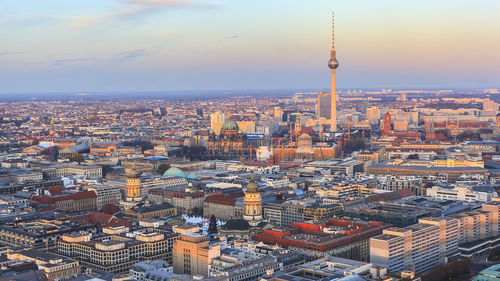 Fernsehturm amidst cityscape against sky during sunset