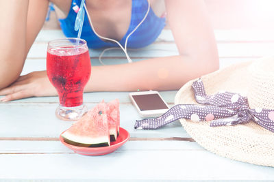 Midsection of woman in bikini relaxing by food and drink on wooden floor