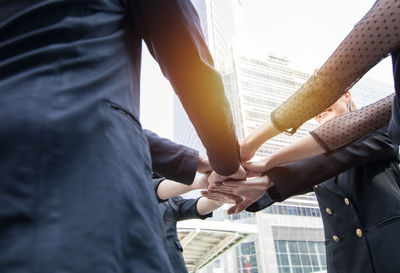 Midsection of colleagues stacking hands in city