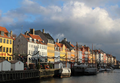 Sailboats moored on river by buildings in city against sky