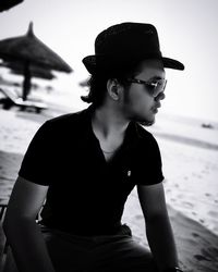 Young man looking away while sitting on beach