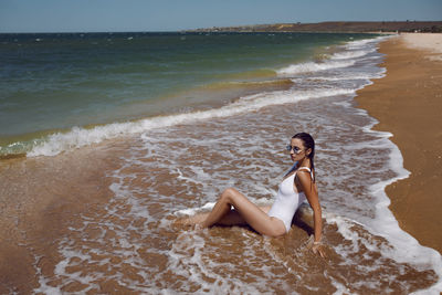 Woman in a white bathing suit and stands on an empty sandy beach
