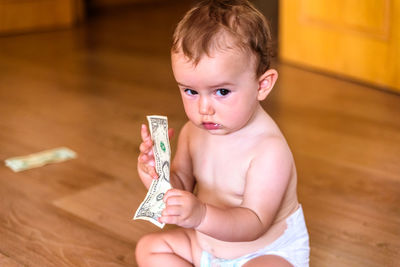 Cute boy holding paper currency while sitting on floor at home