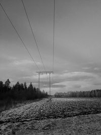 Electricity pylon on field against cloudy sky