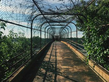 Footbridge in greenhouse against sky