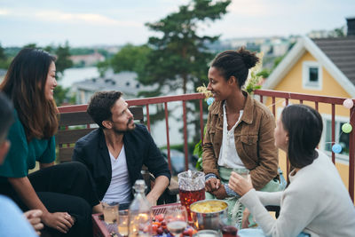 Happy friends talking while sitting on terrace during social gathering