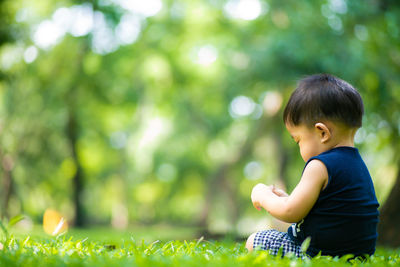 Side view of baby boy sitting on grassy land in park