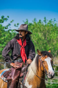 Mature man looking away while sitting on horse at farm