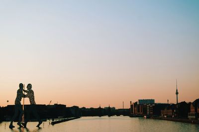 Molecule men on river against clear sky during sunset