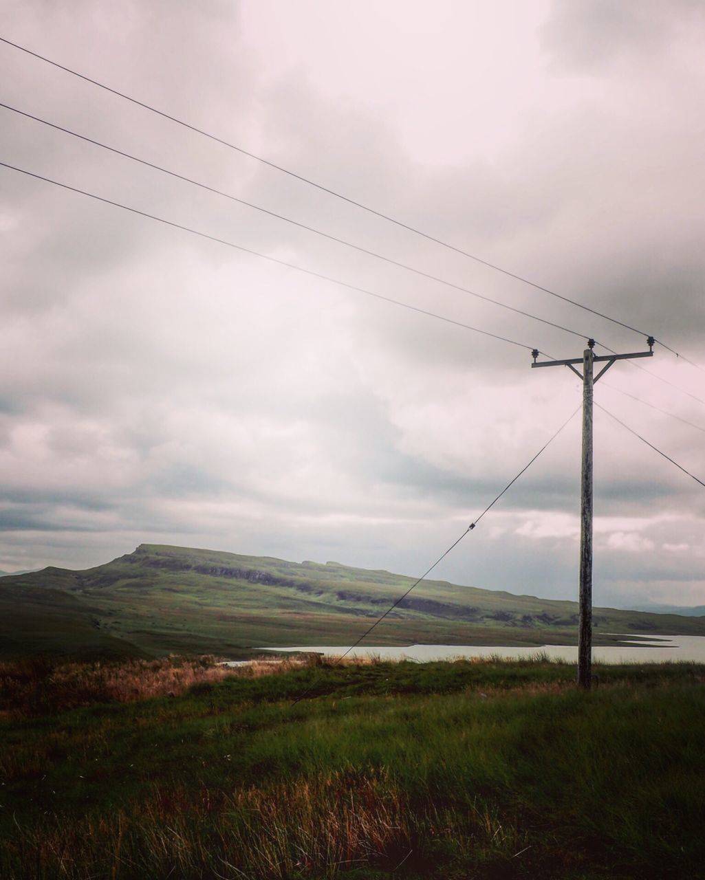 sky, tranquil scene, landscape, scenics, grass, cloud - sky, tranquility, power line, beauty in nature, nature, cable, remote, pole, cloudy, non-urban scene, mountain, outdoors, cloud, day, grassy, growth, green color, tall - high, solitude, no people, rural scene, countryside