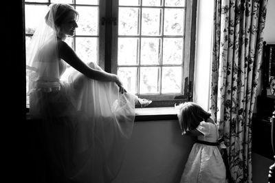 Woman sitting on window sill in wedding dress