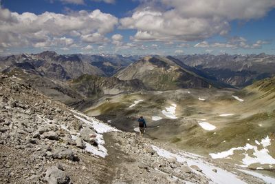 Hiker walking on mountain against cloudy sky