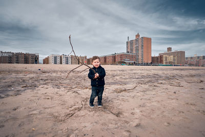 Happy young toddler running around the beach with a big branch