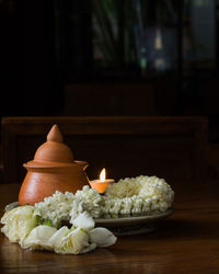 Close-up of mogra garland by illuminated candle and pot on table