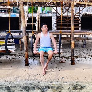 Young man sitting on swing at beach
