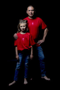 Portrait of siblings standing against black background