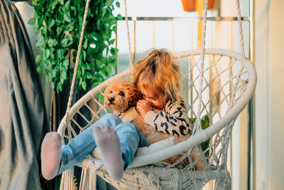 Happy little girl, child hugging with a smile her pet, poodle dog home on balcony in spring sunset.