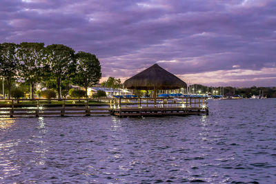 Thatched roof on pier by lake against cloudy sky at dusk