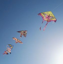 Low angle view of kites flying against clear blue sky