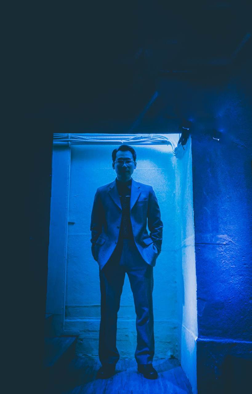 PORTRAIT OF YOUNG MAN STANDING AGAINST BLUE WALL