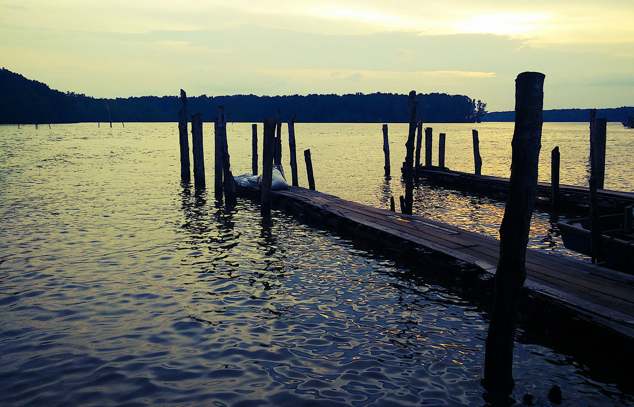 WOODEN POSTS ON PIER AT LAKE AGAINST SKY