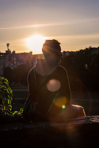 Man sitting in city against sky during sunset