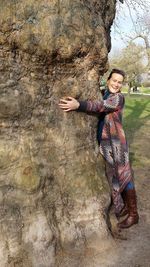 Portrait of woman standing with arm around tree