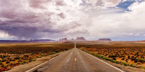 Empty road amidst field against sky