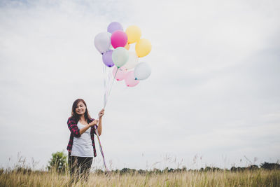 Woman holding balloons on field against sky